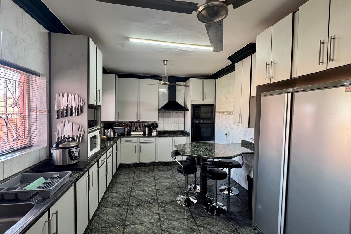 A functional kitchen featuring ample built-in cabinetry, granite countertops, integrated oven, extractor fan, and a breakfast nook area with tiled flooring.