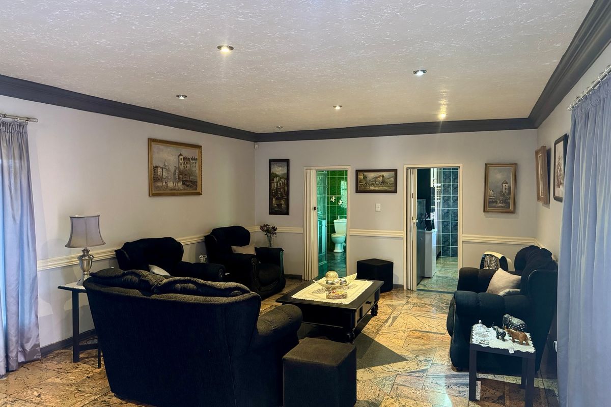 Spacious living room featuring stone tile flooring, crown molding, and recessed lighting, with direct access to adjacent bathroom and utility areas.