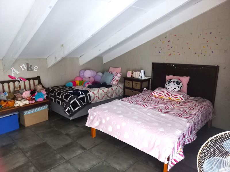 Spacious attic-style bedroom featuring exposed timber rafters, tiled flooring, and exposed blockwork walls, offering a unique architectural character.