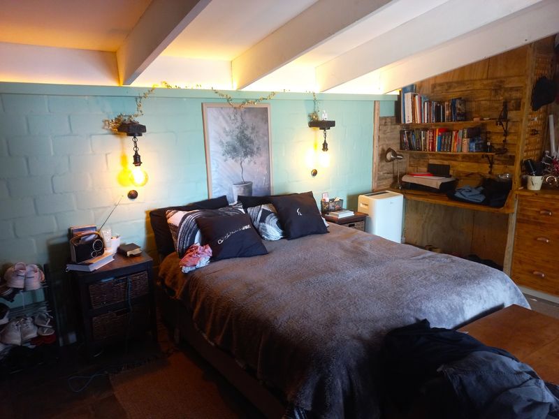 A cozy bedroom featuring exposed ceiling beams, a painted brick feature wall, and integrated wooden shelving with a built-in desk area.