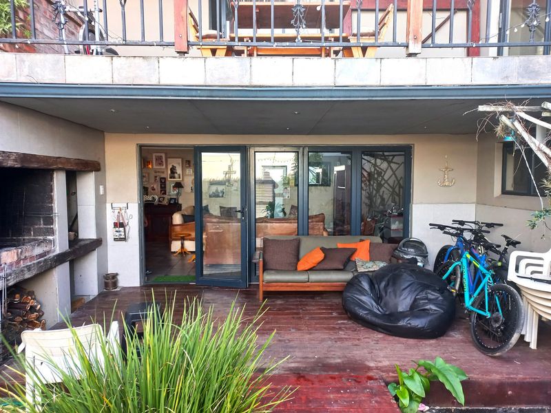 Covered patio area featuring a built-in braai, wooden decking, and direct access to the interior living space through aluminium sliding doors.