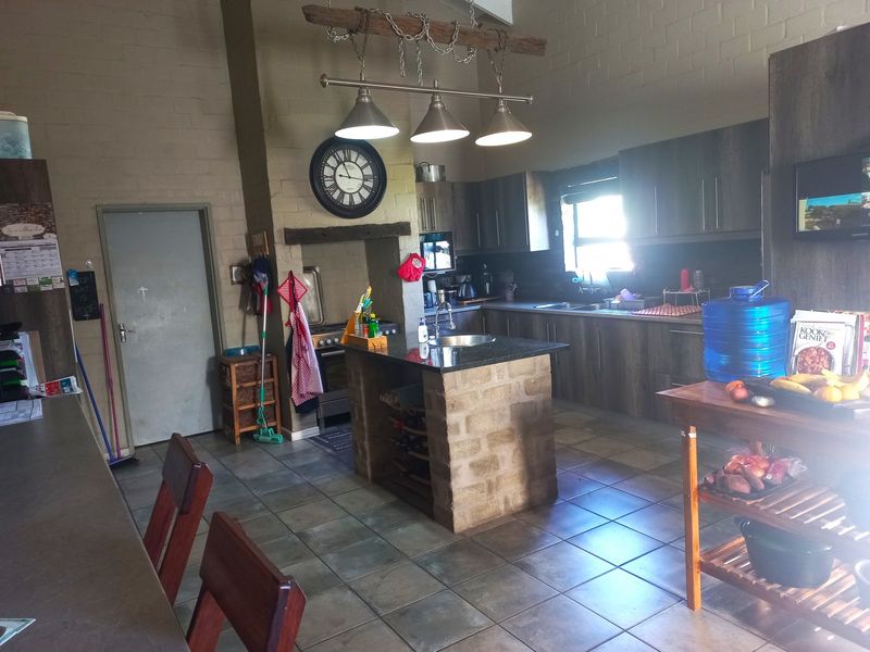 A rustic-style kitchen featuring a central stone-based island, granite countertops, dark wood cabinetry, and tiled flooring under a high vaulted ceiling.