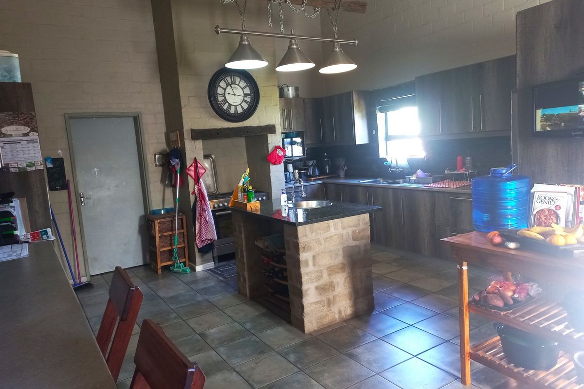 A rustic-style kitchen featuring a central stone-based island, granite countertops, dark wood cabinetry, and tiled flooring under a high vaulted ceiling.