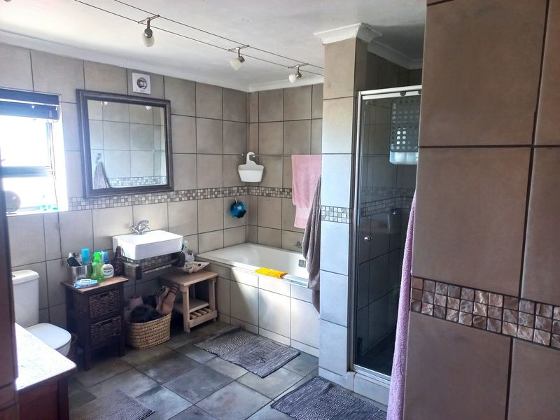 A functional bathroom featuring a built-in bathtub, separate glass shower enclosure, wall-mounted basin, and neutral ceramic tiling throughout.