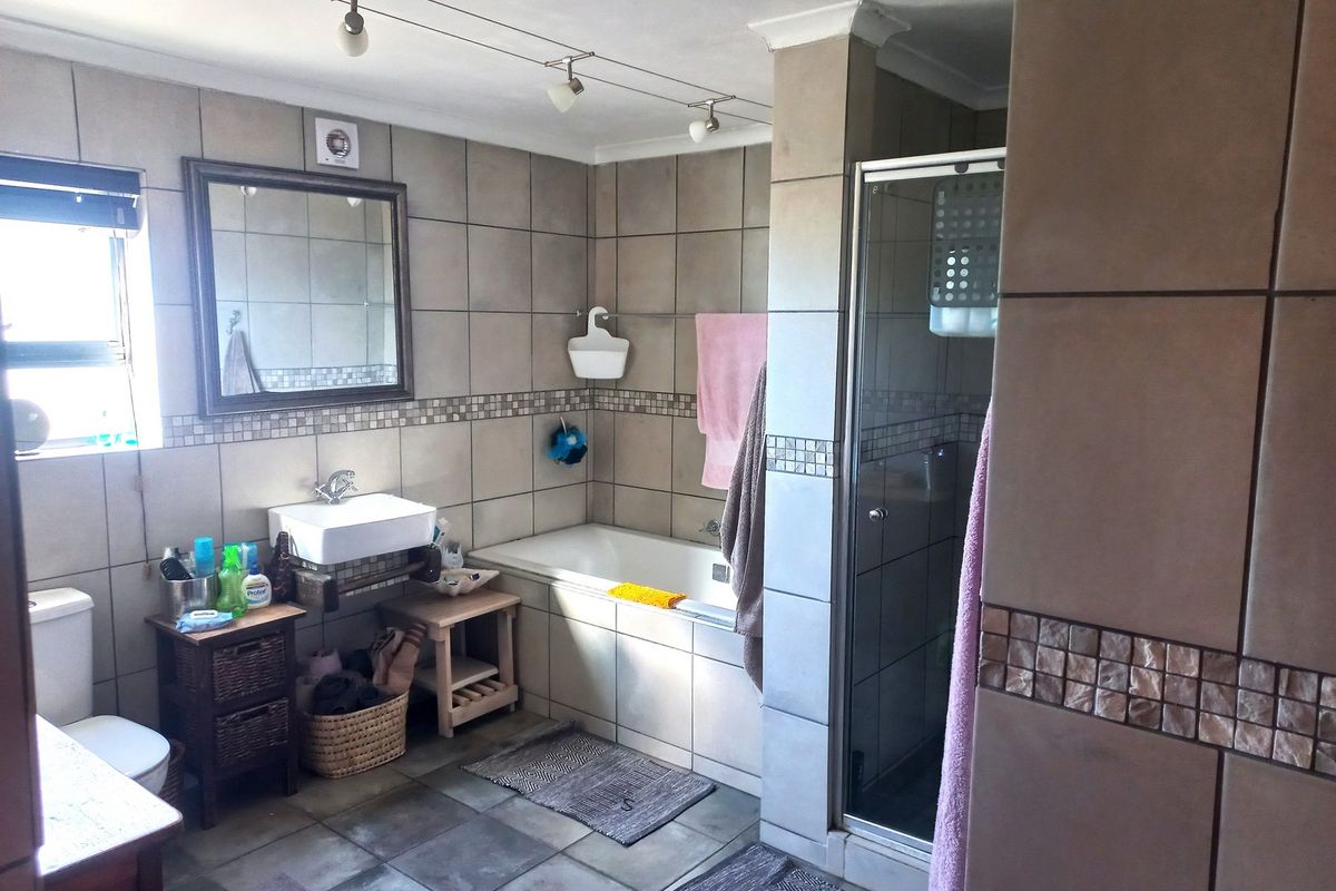 A functional bathroom featuring a built-in bathtub, separate glass shower enclosure, wall-mounted basin, and neutral ceramic tiling throughout.