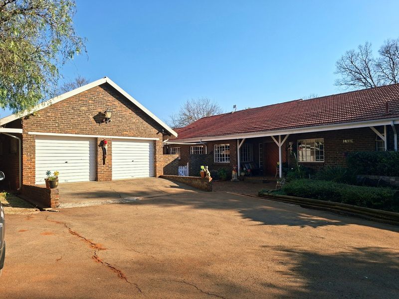 Front view of a brick-faced small holding featuring a double garage, tiled roof, and a paved driveway leading to a covered entrance.