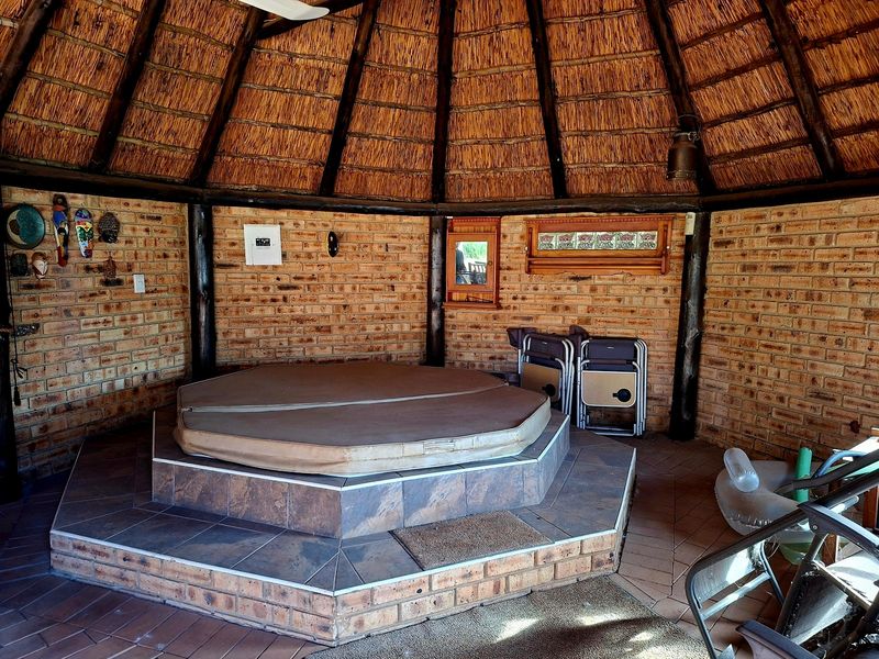 A covered outdoor entertainment area featuring a raised tiled platform with a built-in spa, set under a traditional thatched roof with exposed brick walls.