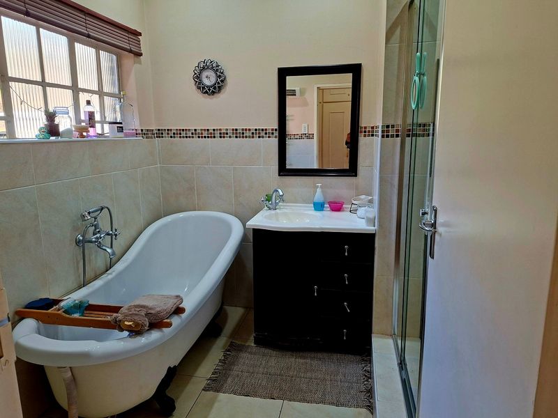 A well-maintained bathroom featuring a classic freestanding bathtub, a vanity with basin, and a separate glass-enclosed shower with neutral wall tiling.
