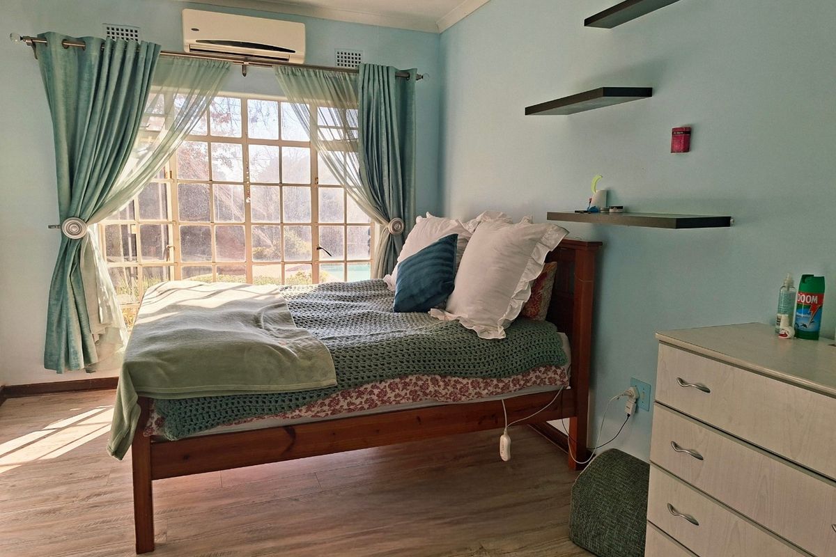 A bedroom featuring laminate flooring, a large window with natural light, and a wall-mounted air conditioning unit.