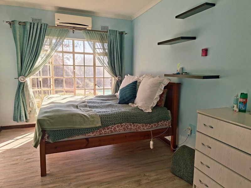 A bedroom featuring laminate flooring, a large window with natural light, and a wall-mounted air conditioning unit.