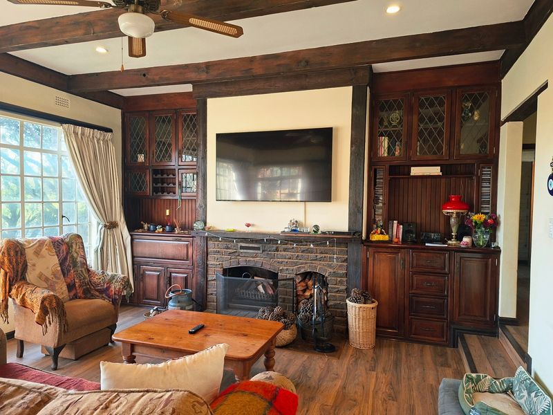 Cozy living room featuring a prominent brick fireplace, custom built-in timber cabinetry, and exposed wooden ceiling beams, creating a warm and traditional atmosphere.
