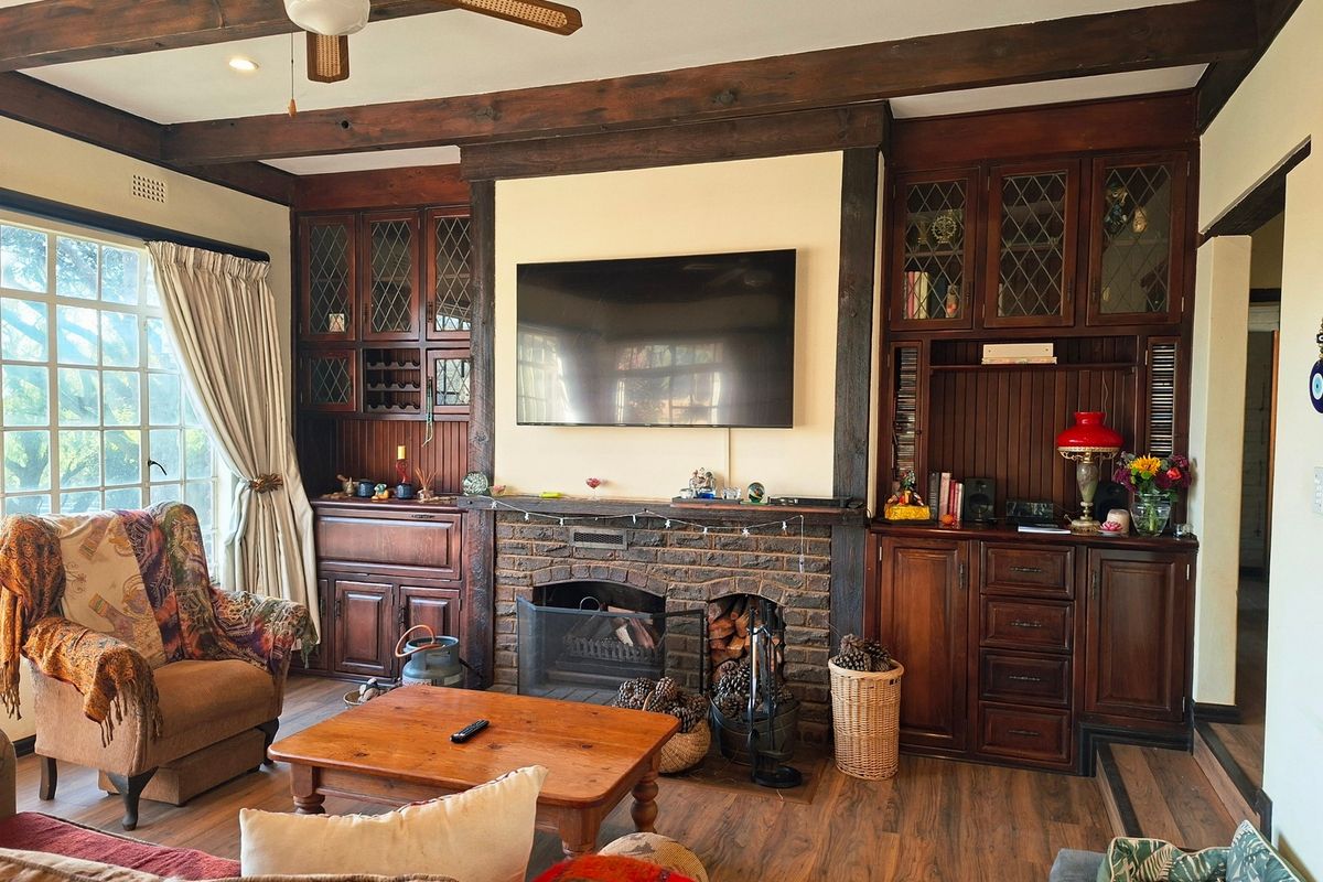 Cozy living room featuring a prominent brick fireplace, custom built-in timber cabinetry, and exposed wooden ceiling beams, creating a warm and traditional atmosphere.