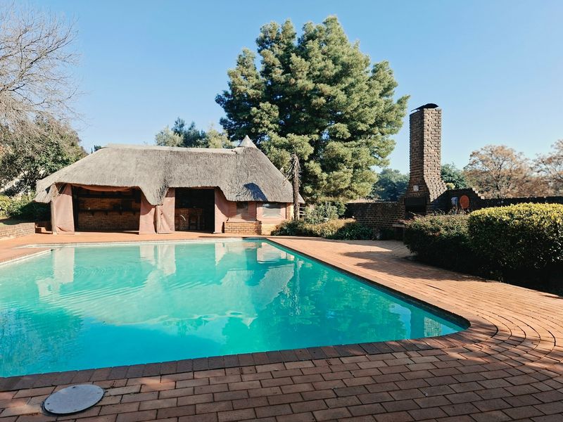 Outdoor pool area featuring a swimming pool, brick paving, and a thatched lapa with a built-in brick braai for entertainment.