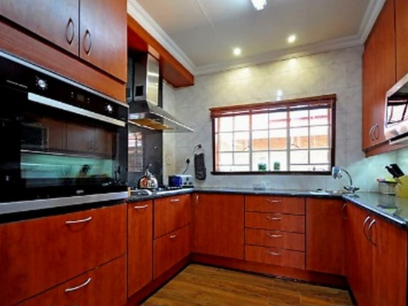 A well-maintained kitchen featuring warm-toned wooden cabinetry, granite countertops, built-in oven, extractor fan, and a tiled backsplash with ample natural light.