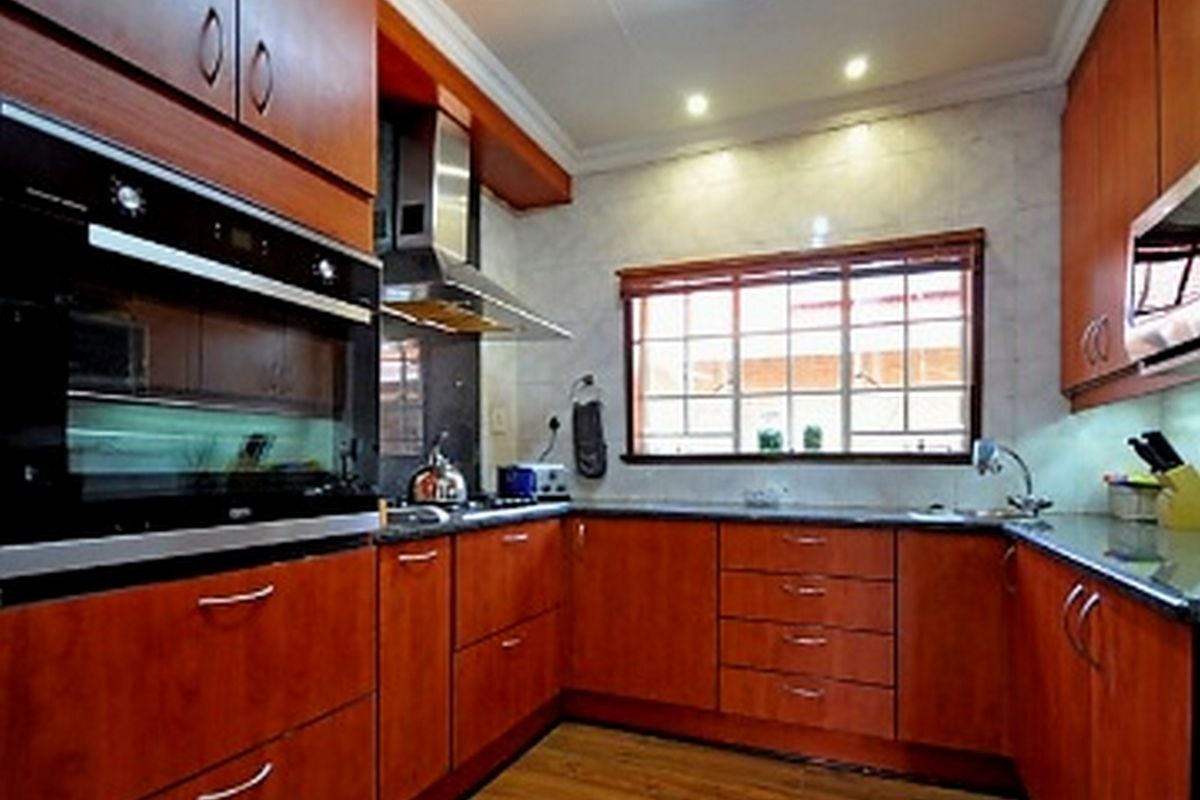 A well-maintained kitchen featuring warm-toned wooden cabinetry, granite countertops, built-in oven, extractor fan, and a tiled backsplash with ample natural light.