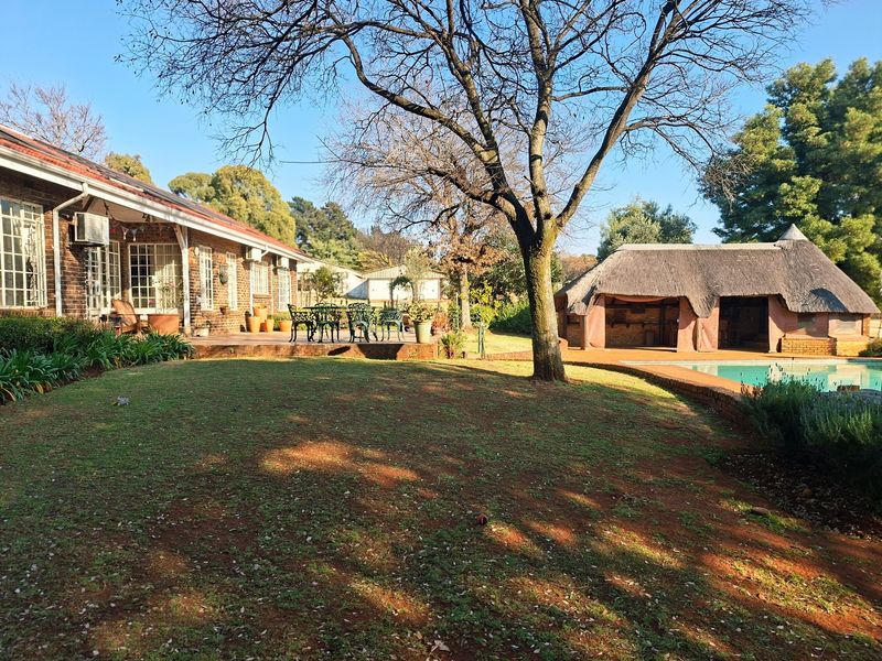Spacious rear garden featuring a brick-built home with a covered patio, a swimming pool, and a traditional thatched lapa entertainment area.