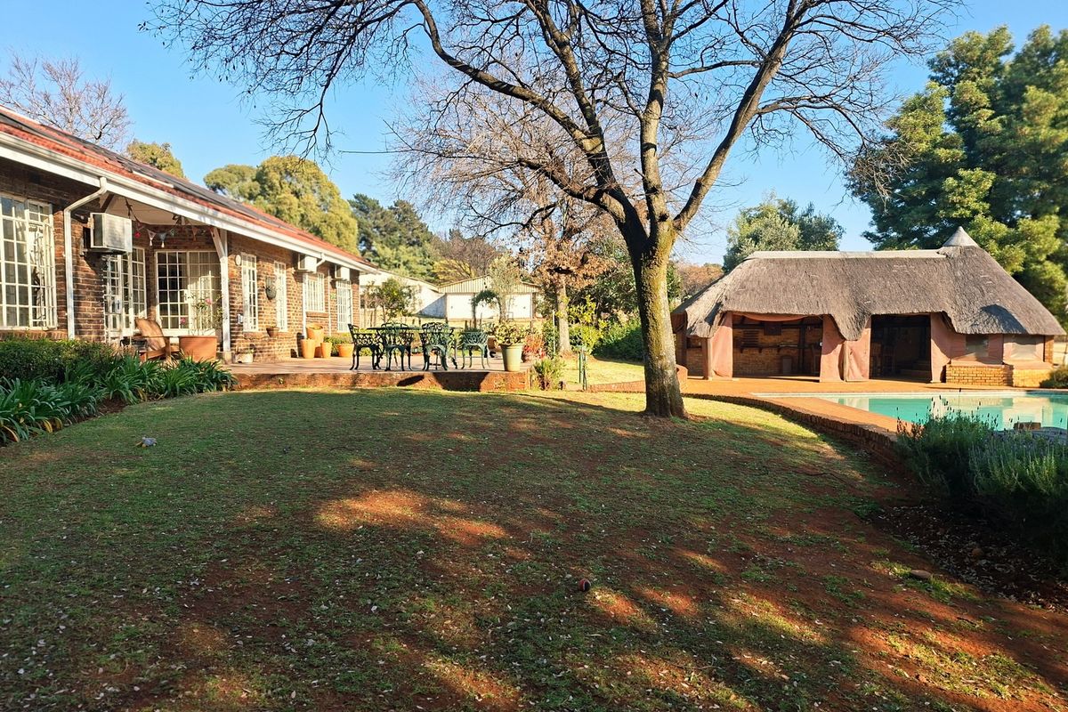 Spacious rear garden featuring a brick-built home with a covered patio, a swimming pool, and a traditional thatched lapa entertainment area.