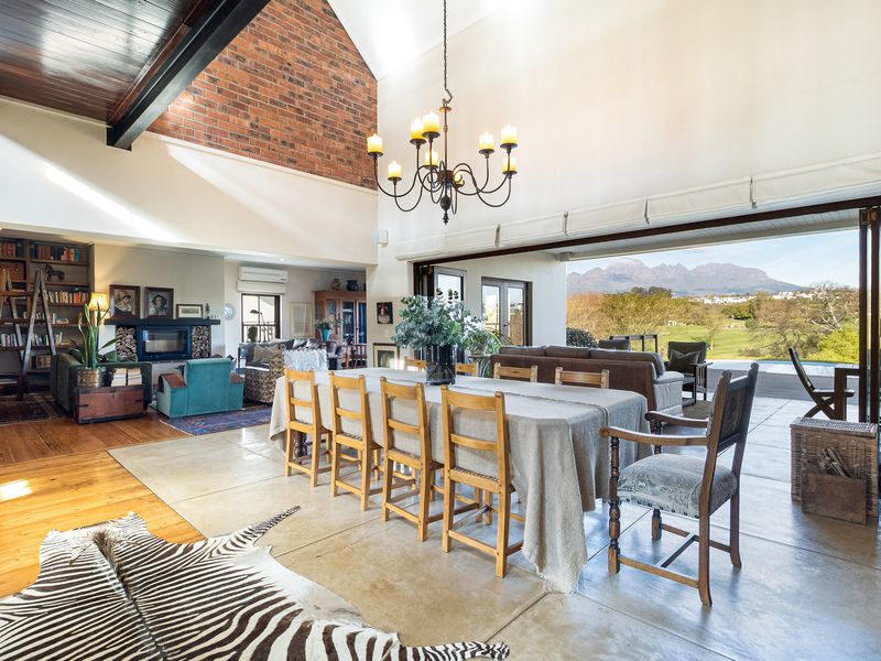Spacious open-plan living and dining area featuring vaulted ceilings, exposed brickwork, polished concrete floors, and seamless indoor-outdoor flow through large bi-fold doors.