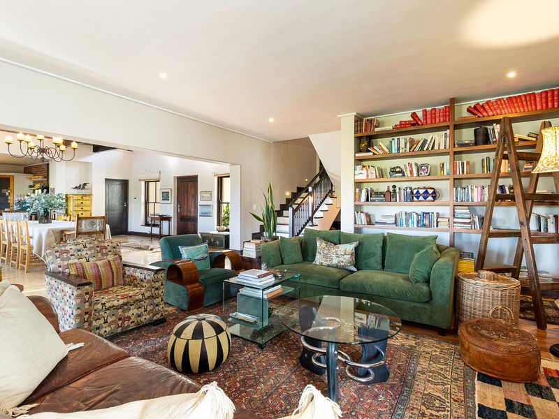 Spacious open-plan living area featuring hardwood floors, a prominent built-in library wall, and an adjoining dining space with a staircase.