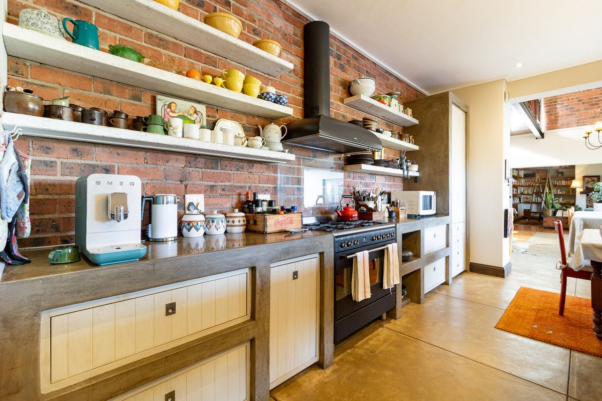 A rustic-style kitchen featuring exposed brick walls, polished concrete countertops, custom cabinetry, and a professional-grade gas stove with an extractor fan.