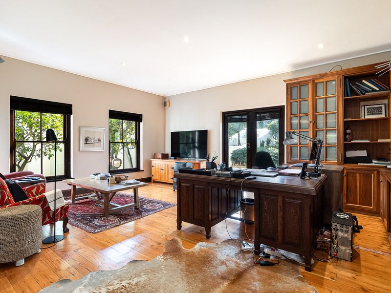 Spacious home office featuring polished timber flooring, extensive built-in wooden cabinetry, and direct access to the garden through glass-paned french doors.