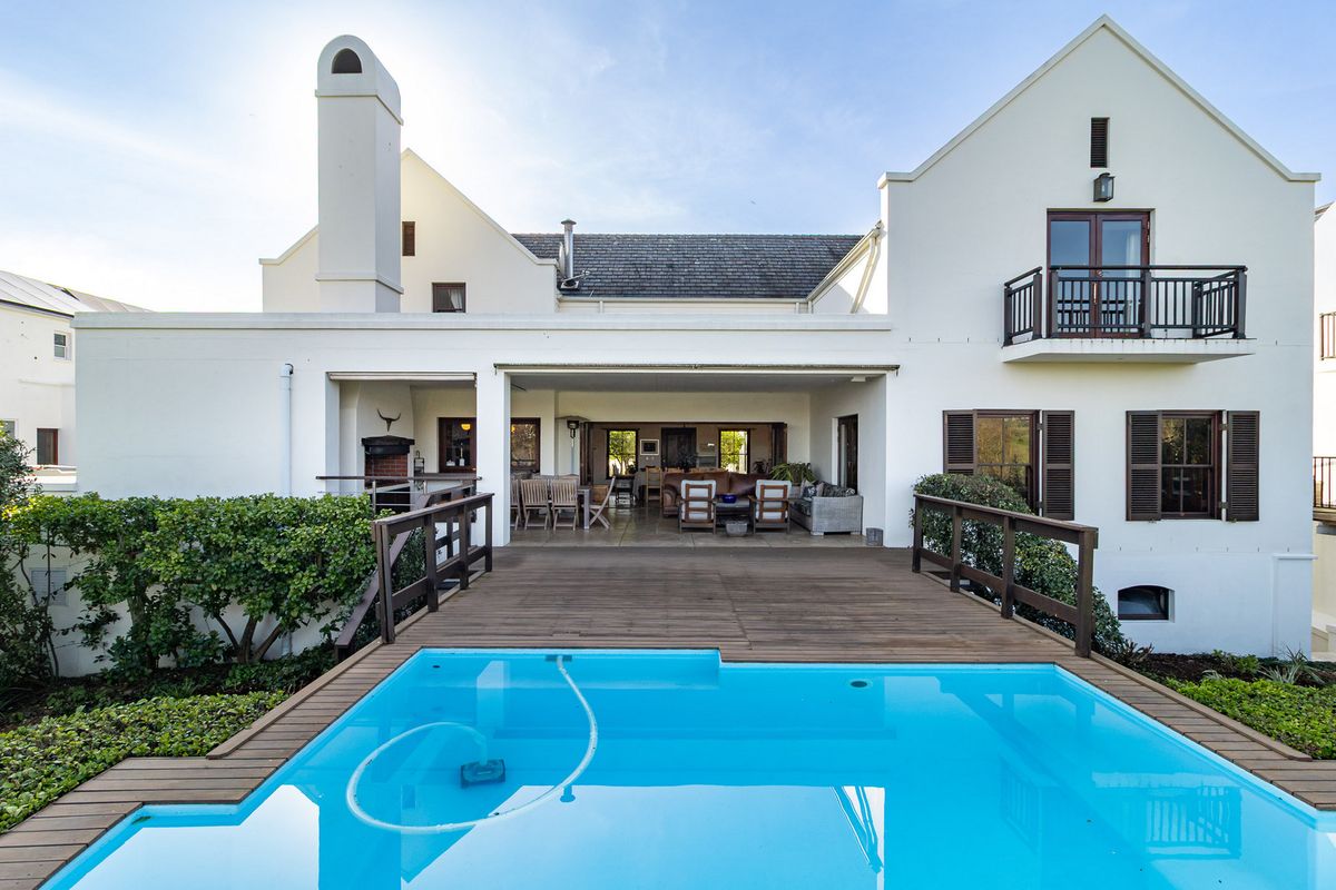 Rear view of the property featuring a swimming pool with timber decking, a covered patio area, and an outdoor fireplace.