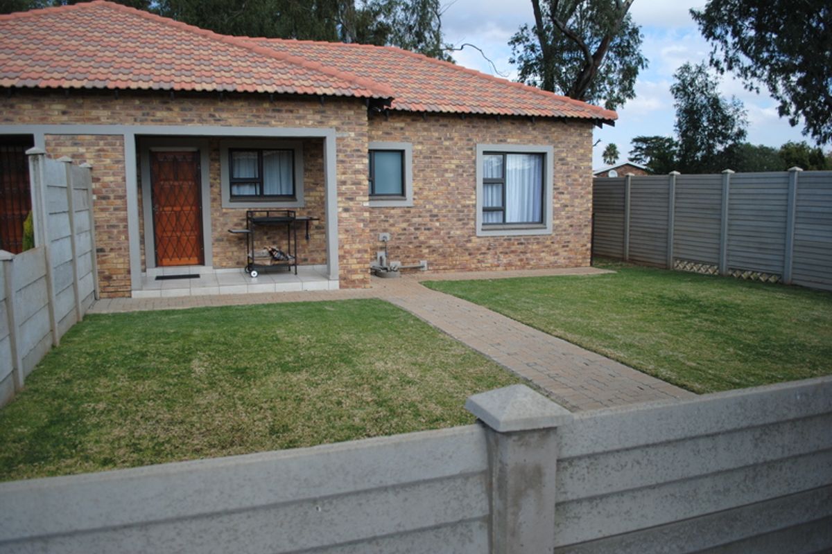 A well-maintained townhouse exterior featuring a face brick facade, tiled roof, covered patio area, and a private garden enclosed by precast concrete boundary walls.