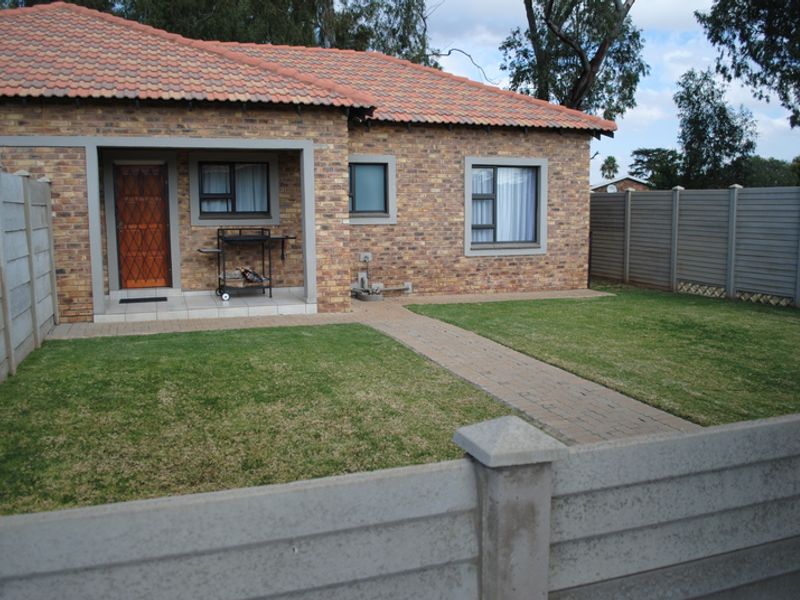 A well-maintained townhouse exterior featuring a face brick facade, tiled roof, covered patio area, and a private garden enclosed by precast concrete boundary walls.