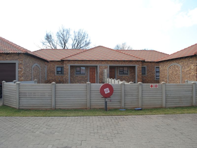 Front view of a face brick townhouse complex featuring tiled roofs, paved driveway, and secure precast concrete boundary walling.