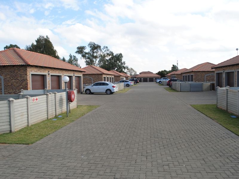 A view of the townhouse complex driveway featuring brick-faced units with tiled roofs, paved access, and individual garage doors.