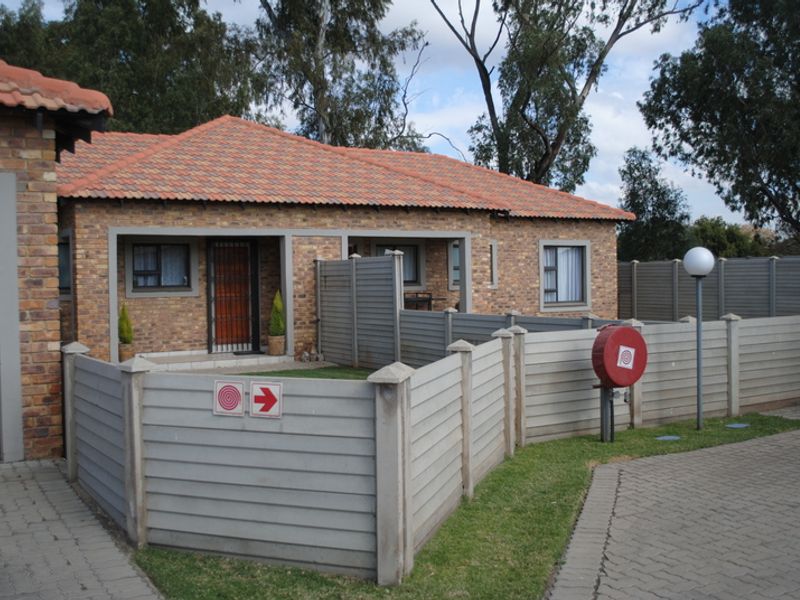 Front view of a face brick townhouse featuring a tiled roof, paved driveway, and secure boundary wall with integrated fire safety equipment.