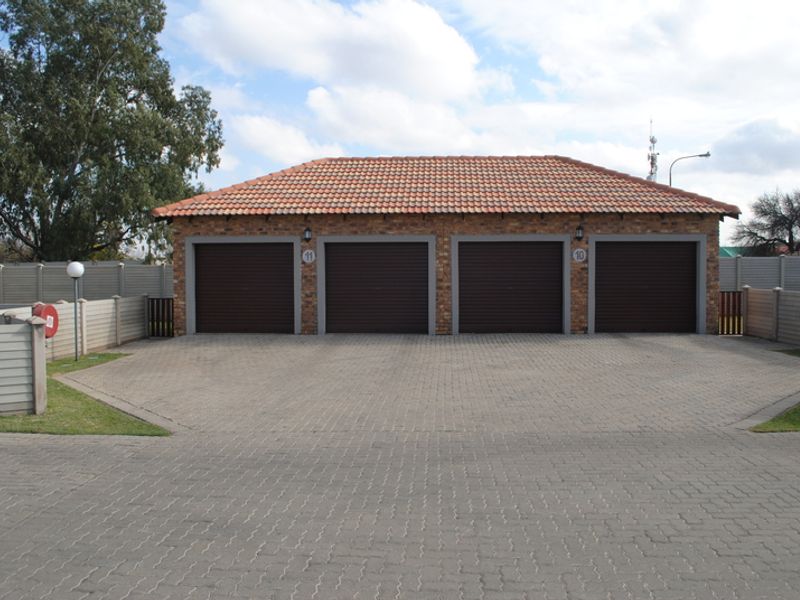 A well-maintained four-car garage block featuring brick construction, tiled roofing, and individual roll-up doors, set within a paved driveway area.
