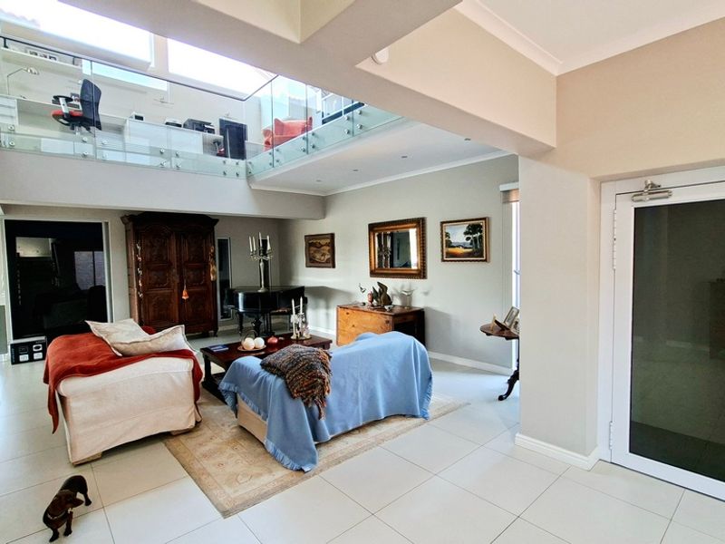 Spacious open-plan living area featuring a mezzanine level with glass balustrades, tiled flooring, and abundant natural light from overhead skylights.