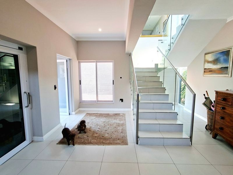 Spacious entrance hall featuring modern tiled flooring, a sleek staircase with glass balustrade, and neutral wall finishes.