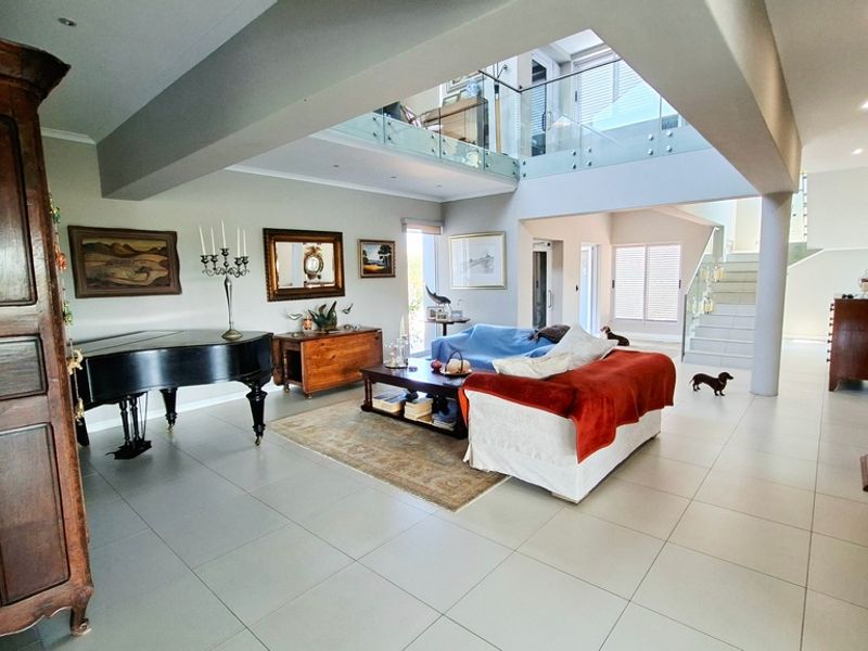 Spacious open-plan living area featuring high ceilings, a mezzanine level with glass balustrades, modern tiled flooring, and recessed lighting.