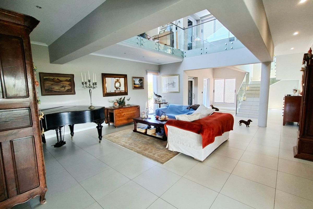 Spacious open-plan living area featuring high ceilings, a mezzanine level with glass balustrades, modern tiled flooring, and recessed lighting.