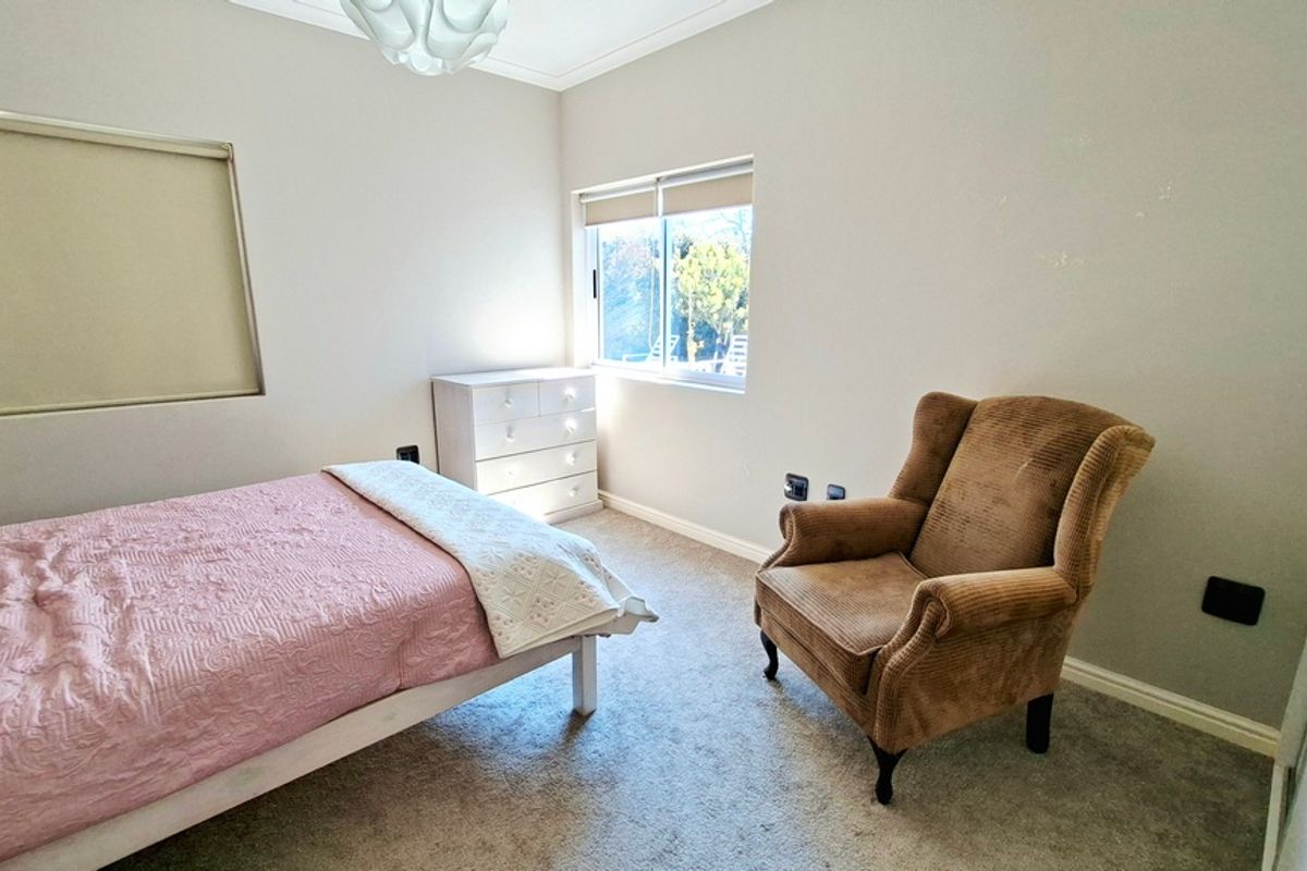 A functional bedroom featuring carpeted flooring, a sliding window with a roller blind, and neutral wall finishes.