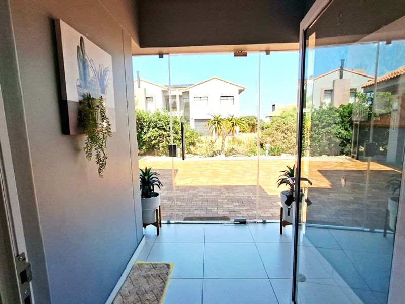 Modern entrance hall featuring large format floor tiles and a seamless glass pivot door opening to the exterior paved area.