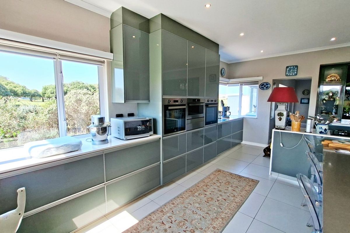 Modern kitchen featuring high-gloss cabinetry, integrated appliances, stone countertops, and large windows providing ample natural light and garden views.