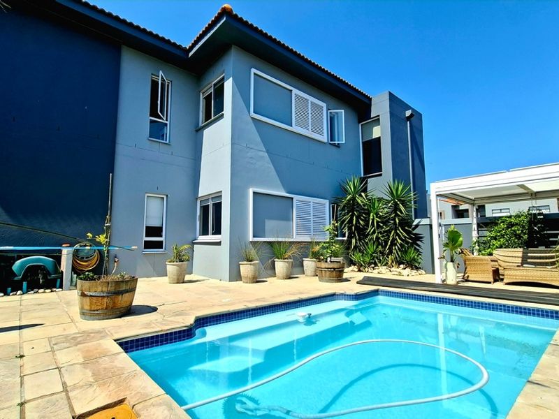 Rear exterior view featuring a swimming pool, paved patio area, and a covered pergola structure attached to the main house.