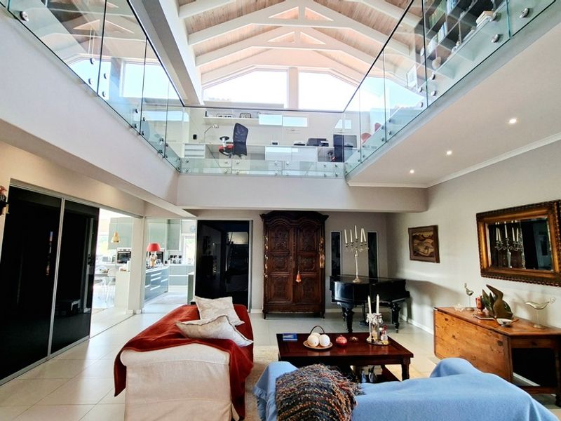 Spacious living area featuring a dramatic double-volume vaulted ceiling with exposed beams, a glass-railed mezzanine level, and modern recessed lighting.