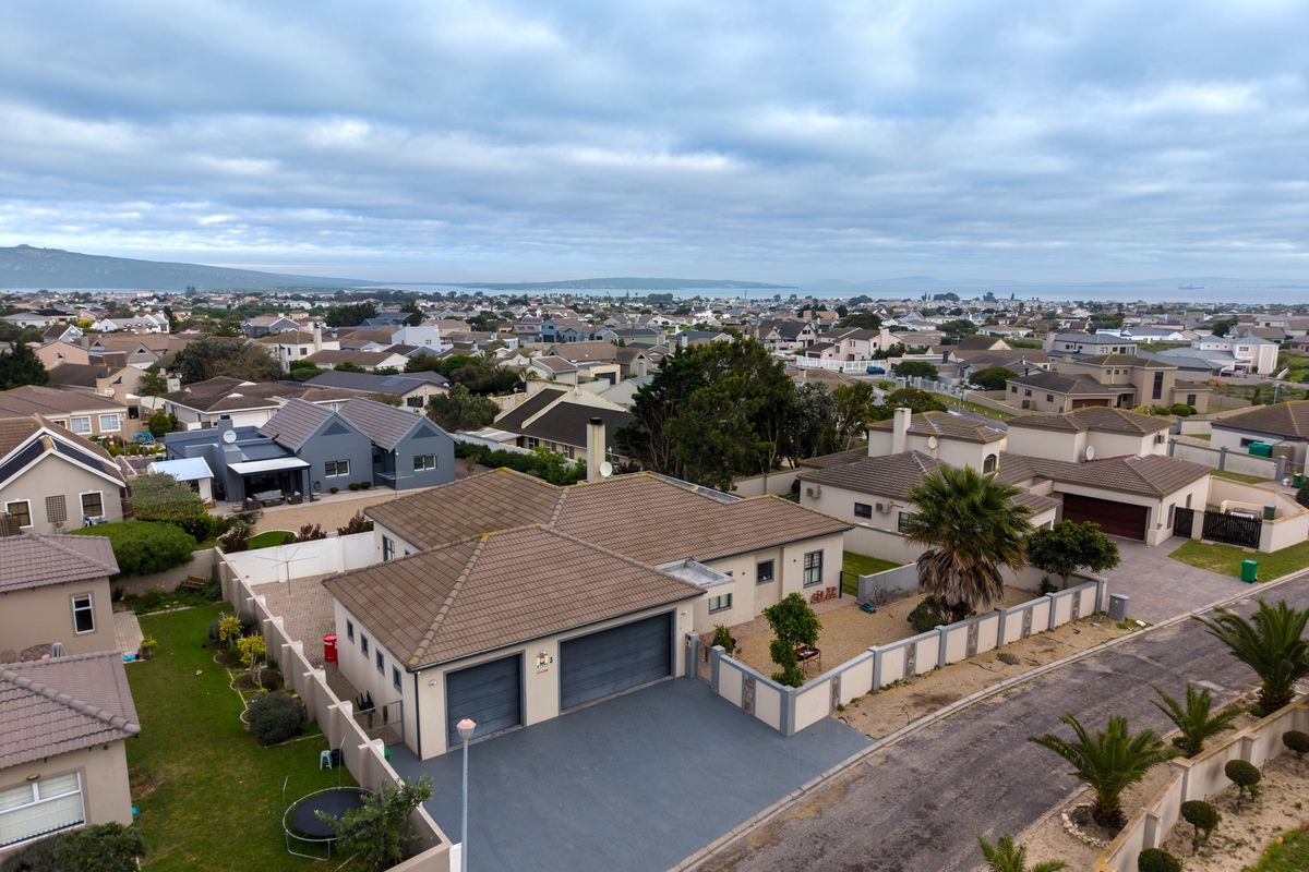 Aerial view of a residential property featuring a double garage, paved driveway, and surrounding boundary walls in a suburban neighborhood setting.