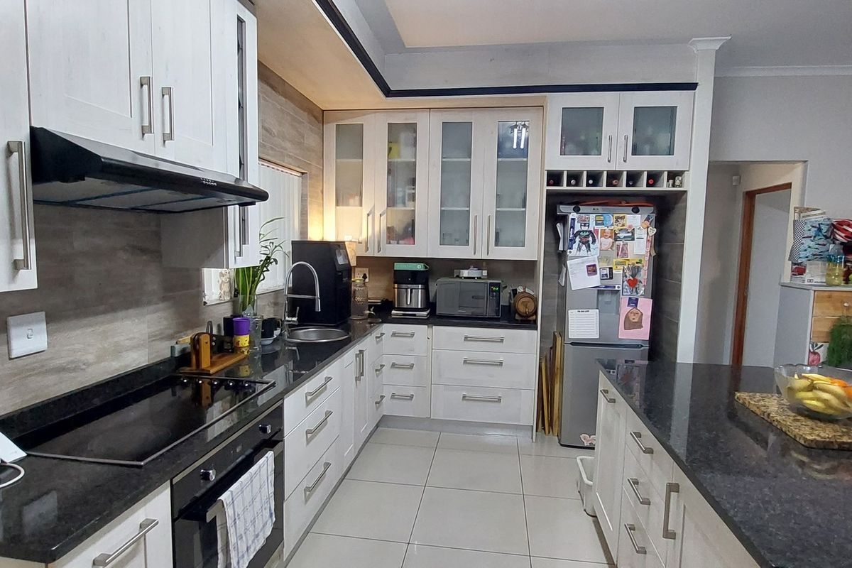 A functional kitchen featuring granite countertops, built-in oven, electric hob, extractor fan, and a central island with ample cabinetry and tiled flooring.