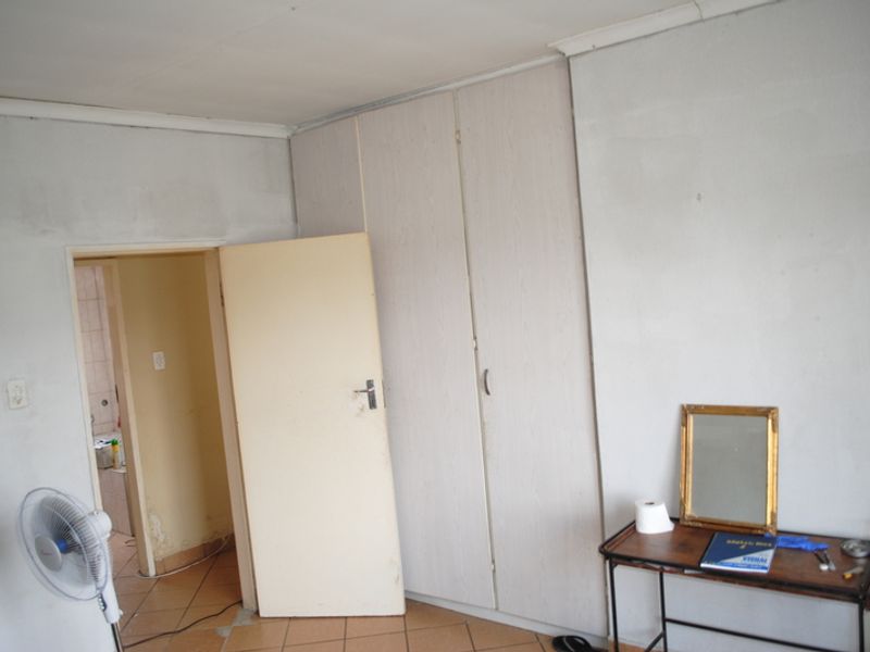 A bedroom featuring built-in cupboards and tiled flooring, requiring cosmetic updates to the walls and finishes to improve its overall appeal.