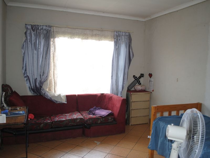 A bedroom featuring tiled flooring and a large window, currently showing signs of wear including cracked plaster and peeling paint.