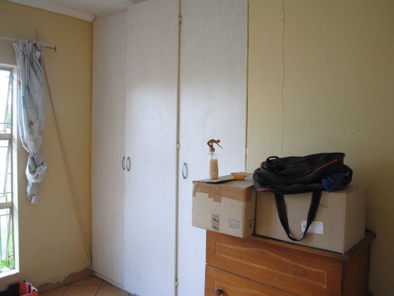 A bedroom featuring built-in cupboards and a window with security bars, showing signs of wear including wall cracks and peeling paint.