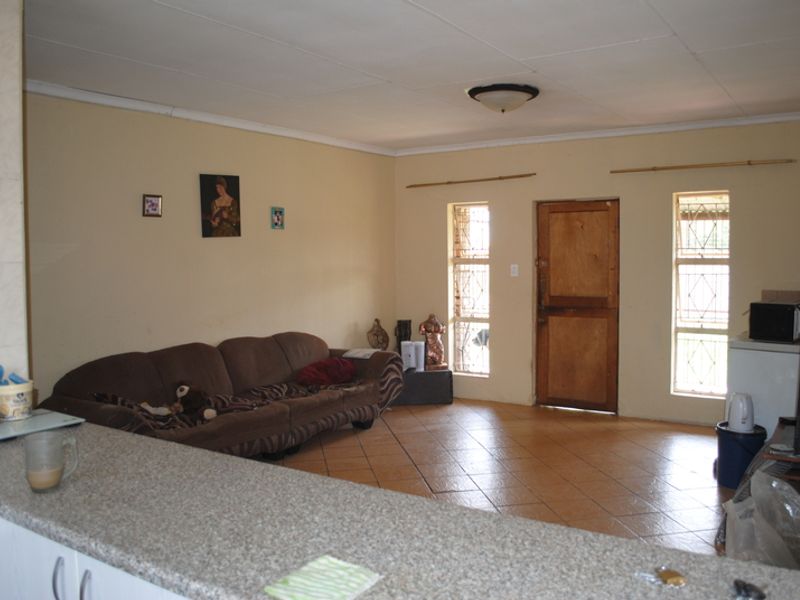 Open plan living area featuring tiled flooring, a kitchen breakfast bar, and natural light through windows with security bars.