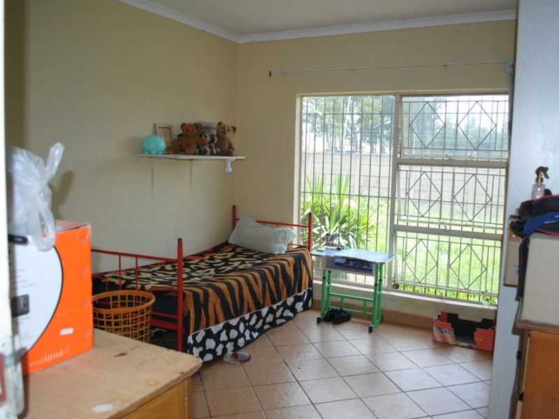 A bedroom featuring tiled flooring and a large window fitted with security bars, providing natural light and views of the exterior.