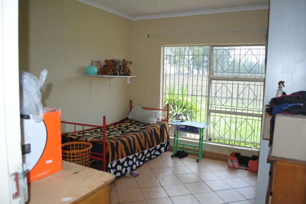 A bedroom featuring tiled flooring and a large window fitted with security bars, providing natural light and views of the exterior.