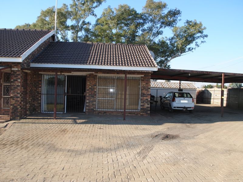 Front exterior view of a brick house featuring a tiled roof, security gates, and an attached carport with a paved driveway.